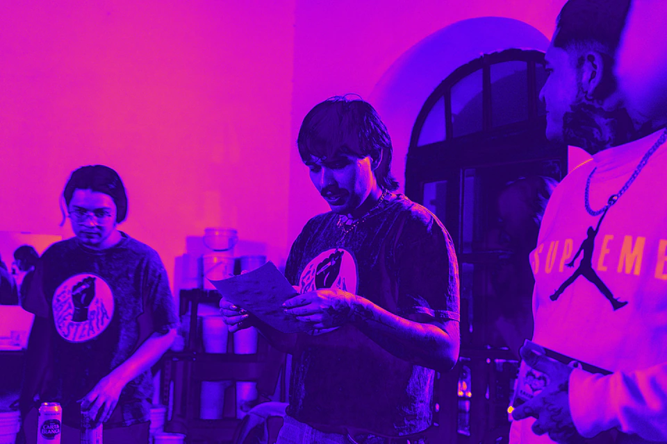 Dos personas con playeras de La Testería leen hojas impresas durante un evento.